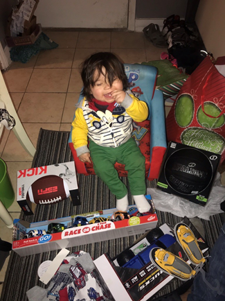 happy young child sitting on the floor surrounded by Christmas gifts